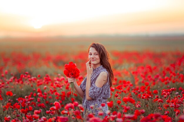 une fille dans un champ avec des coquelicots dans ses mains sourit