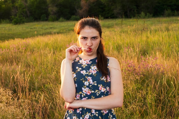 Une fille dans un champ jaune d'été mange des bonbons sur un bâton et fronce les sourcils avec émotion.