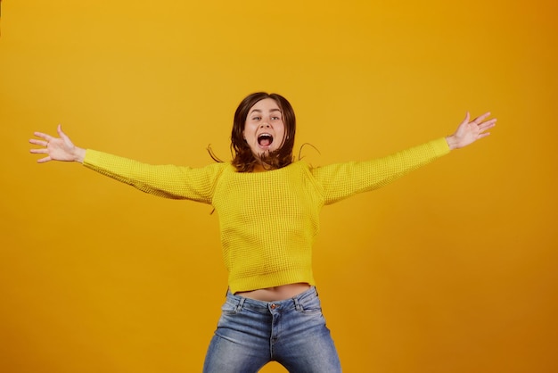 La fille dans un chandail jaune se réjouit sur un fond jaune