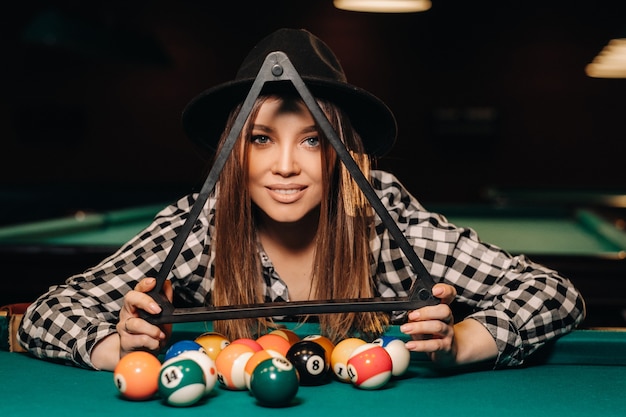 Une fille dans un chapeau dans un club de billard avec des boules dans ses mains