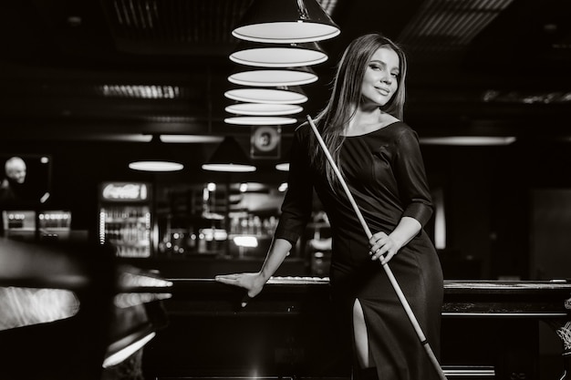 Une fille dans un chapeau dans un club de billard avec une queue dans ses mains.billard Game.black et photo blanche.