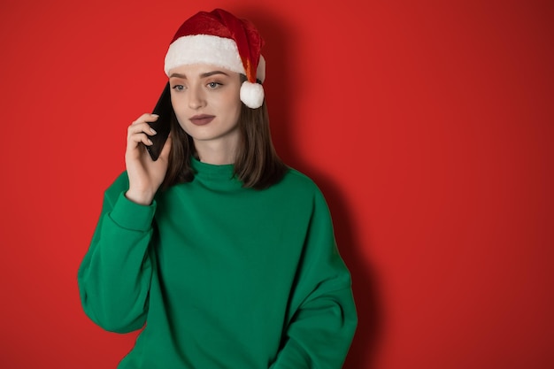 Une fille dans un chapeau du Nouvel An parle au téléphone sur un fond uni tenant un téléphone dans sa main en commandant le dîner le concept du week-end du Nouvel An 2023 joyeuses fêtes de Noël 2023