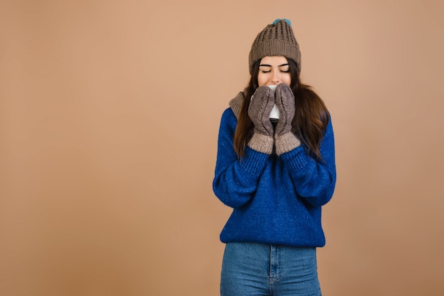 Fille dans un chapeau et des gants tenant une tasse. Isolé sur fond marron