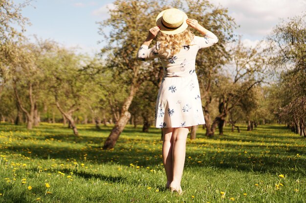 Fille dans un chapeau de paille dans le jardin. Vue arrière. Tenue d'été ou de printemps décontractée à la mode