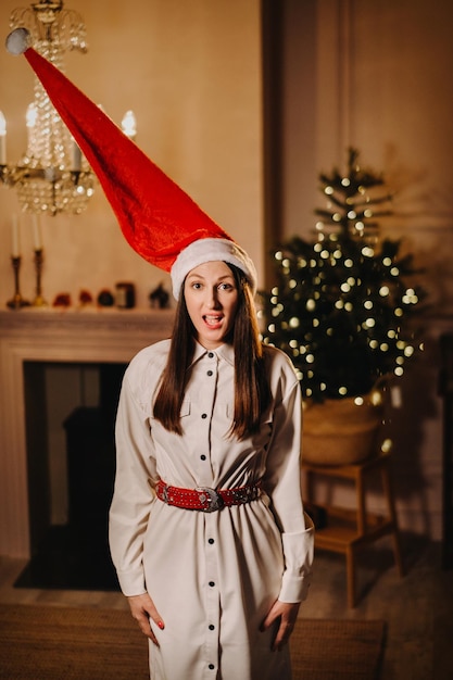 Une fille dans un chapeau de père Noël se tient à la maison la veille de Noël