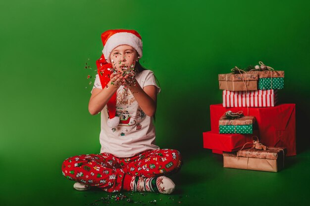 une fille dans un chapeau de père Noël soufflant des confettis sur un fond vert pour le texte