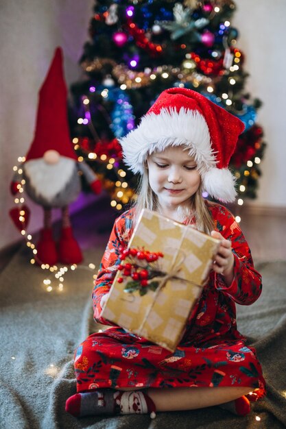 Une fille dans un chapeau de père noël trie des cadeaux dans le contexte d'un arbre de Noël