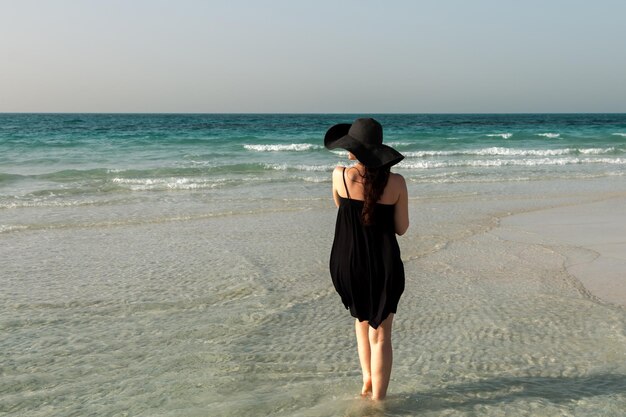 Une fille dans un chapeau et une robe noirs se tient sur le fond de la mer