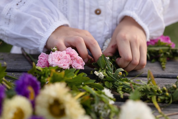 Une fille dans une chemise ample blanche fait une couronne de fleurs sauvages colorées