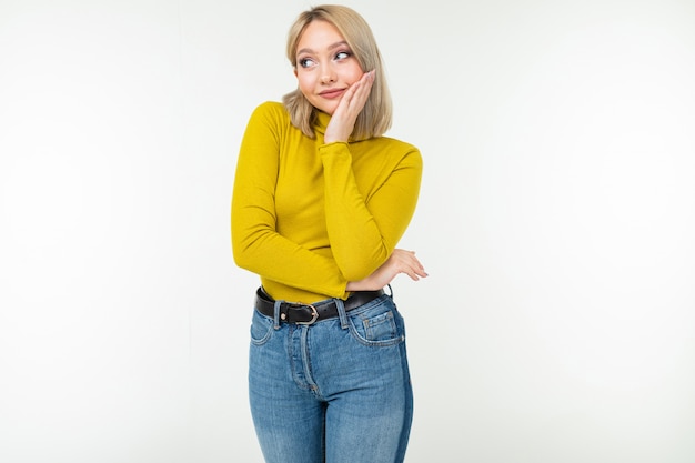 Fille dans un chemisier jaune et un jean regarde pensivement un fond de studio blanc