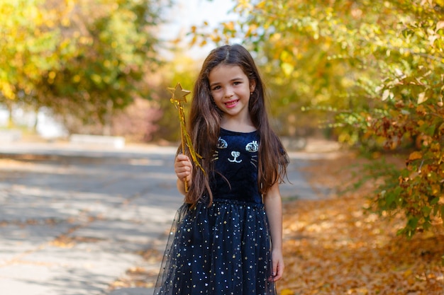 Fille dans un costume de sorcière avec une baguette magique pour Halloween à l'automne parc