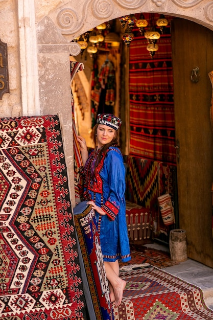 Fille dans un costume turc national bleu photographié dans un magasin de tapis