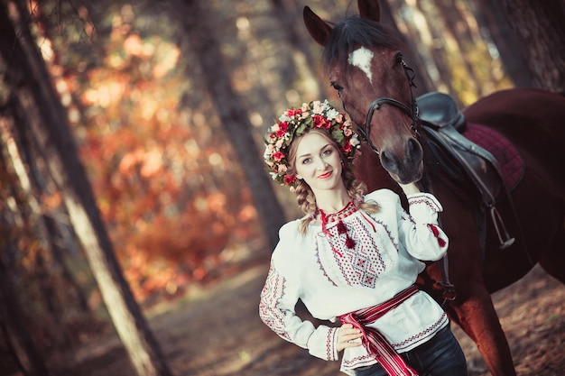 Fille dans une couronne et chemise brodée avec un cheval en forêt