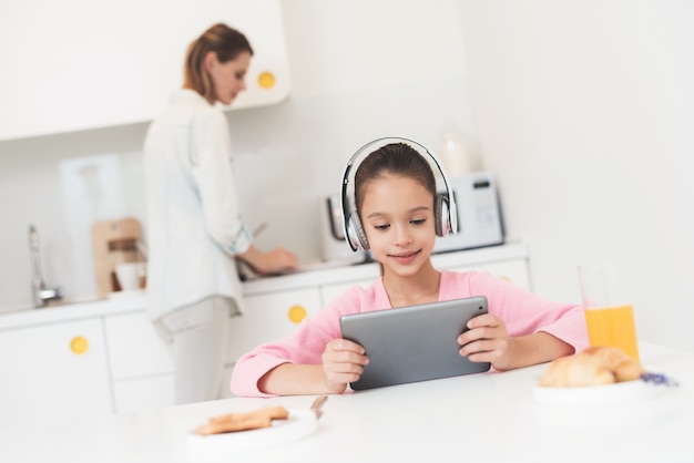 Fille dans les écouteurs et tablette est assis dans la cuisine