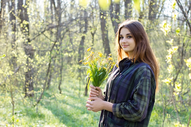 Fille dans la forêt avec un bouquet de fleurs jaunes.