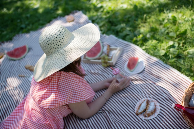 Une fille dans un grand chapeau de paille est allongée sur la plage, en pique-nique.