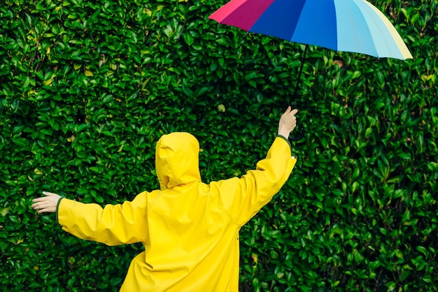 Fille dans un imperméable jaune sur un fond de mur avec de l'herbe avec un parapluie multicolore