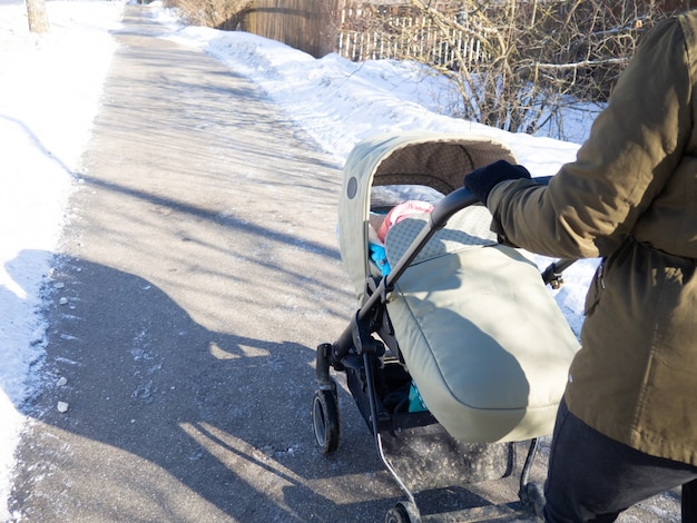 Une fille dans un jour glacial d'hiver roule une poussette de bébé avec un enfant