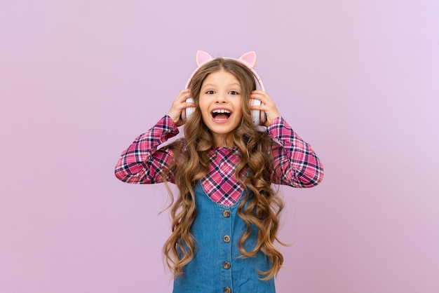 Une fille dans une jupe en jean et une veste à carreaux écoute de la musique avec des écouteurs L'enfant est content des nouveaux écouteurs