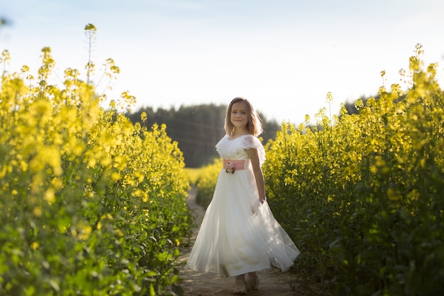 fille dans une longue robe blanche dans un champ de colza en été