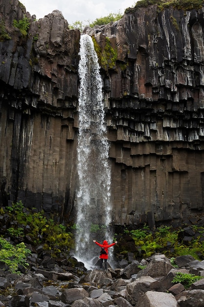 Une fille dans une longue veste rouge près de la cascade Svartifoss Parc National de Vatnajokull Islande