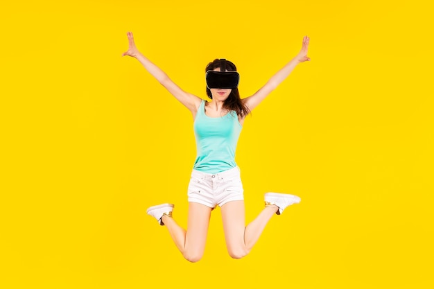 Fille dans des lunettes VR de réalité virtuelle saute sur un mur jaune