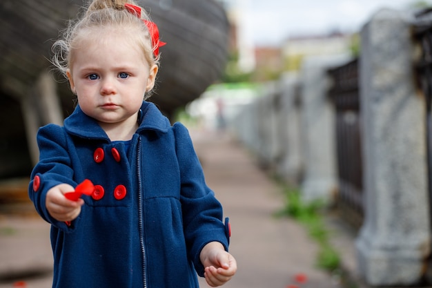 Fille dans un manteau bleu et un arc rouge est assise dans la rue de la ville