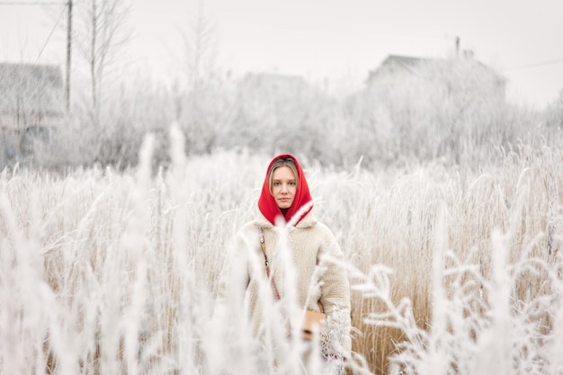 Une fille dans un manteau de fourrure blanc et un sweat à capuche brillant pose dans des buissons enneigés