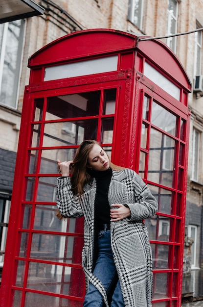 Une fille dans un manteau gris se tient près d'une cabine téléphonique rouge