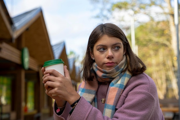 Fille dans un manteau mange de la nourriture de rue debout à une table dans un café en plein air