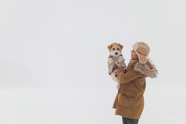 Une fille dans un manteau marron et un jack russell terrier se tiennent sur un fond blanc pendant un blizzard Le chien est assis sur les mains d'un homme Concept de Noël