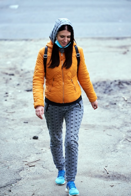 Une fille dans un masque médical, à capuche avec une mallette dans une veste orange, va de l'avant. Sourires