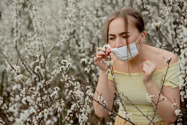 Fille dans un masque médical. Fille au printemps parmi le jardin fleuri. Une fille dans un masque médical de protection. Concept d'allergie au printemps.