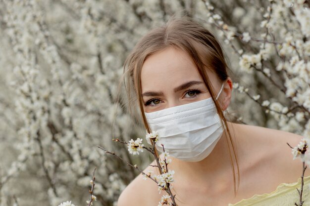 Fille dans un masque médical. Fille au printemps parmi le jardin fleuri. Une fille dans un masque médical de protection. Concept d'allergie de printemps