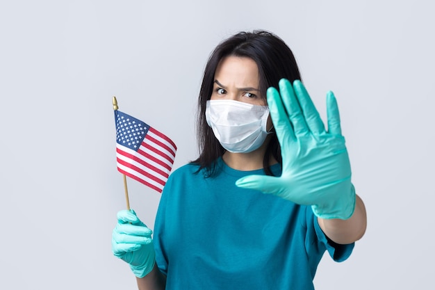 Une fille dans un masque médical et des gants tient un drapeau américain dans ses mains Concept de coronavirus