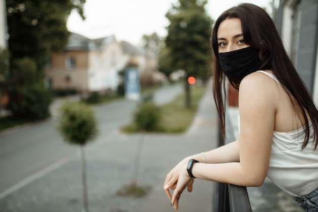 Fille dans un masque de protection sur un balcon regarde une ville vide