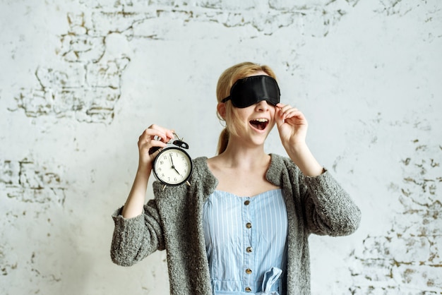 Fille dans un masque de sommeil tient un réveil à la main