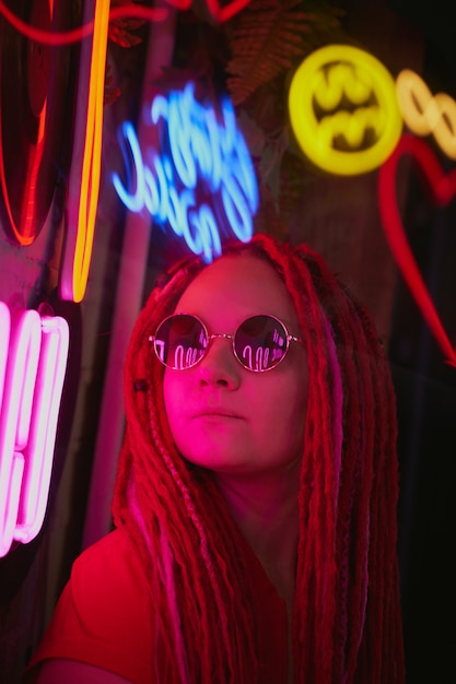 Fille dans des néons, belle femme à lunettes de soleil, aux cheveux roses, avec des nattes de dreadlocks,