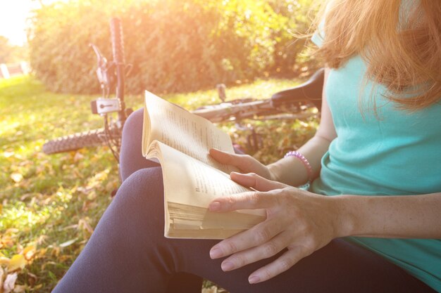 Photo une fille dans le parc est assise sous un arbre et lit un livre. à côté il y a un vélo et un sac à dos