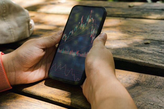 Fille dans le parc tenant un smartphone avec graphique boursier financier sur l'écran Table en bois rustique