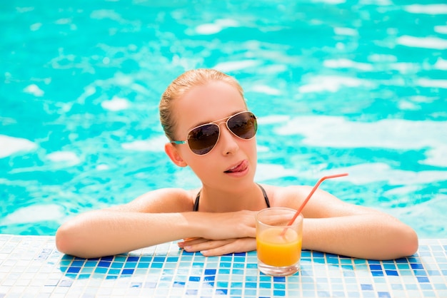 fille dans une piscine avec du jus et des verres montrant la langue