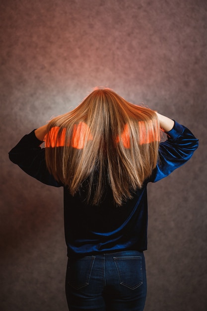 Fille dans un pull bleu sur fond gris. Avoir de beaux cheveux et elle pose magnifiquement