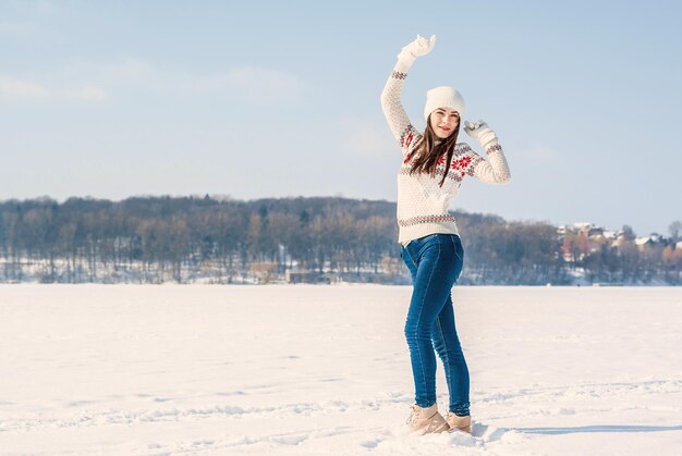 Une fille dans un pull d'hiver blanc danse sur la glace enneigée d'un lac gelé