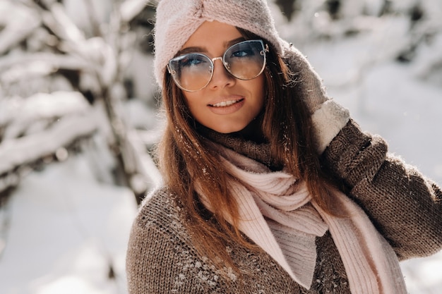 Une fille dans un pull et des lunettes en hiver dans une forêt couverte de neige