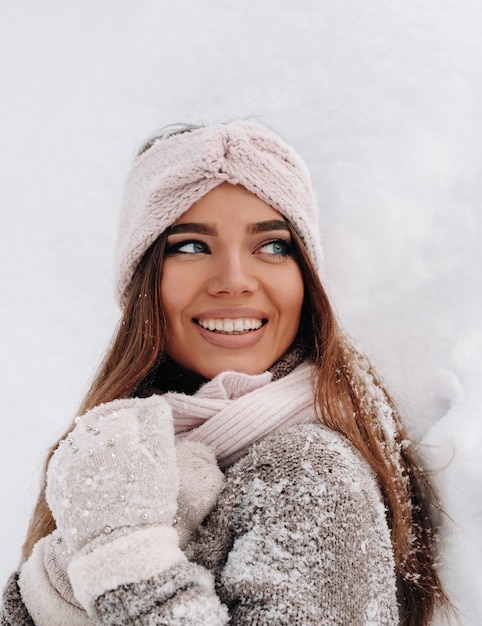 Une fille dans un pull et des mitaines en hiver se dresse sur un fond couvert de neige.