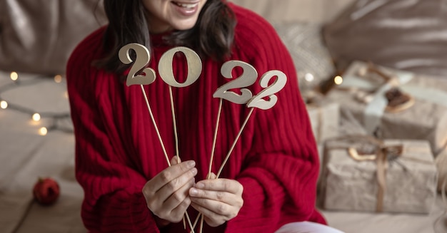 Photo fille dans un pull rouge détient des numéros en bois 2022 sur des bâtons, arrière-plan flou avec bokeh.