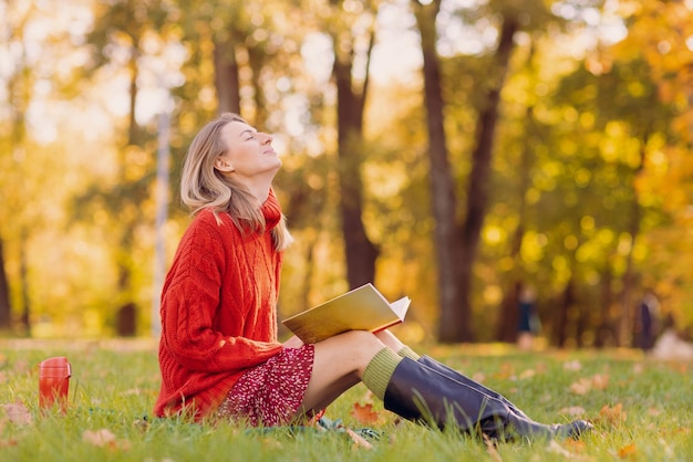 une fille dans un pull rouge lit un livre dans le parc d'automne le concept de la saison d'automne