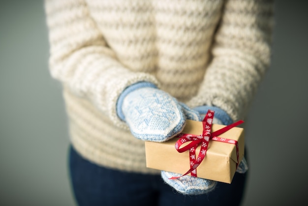 Une fille dans un pull tricoté chaud et des mitaines tient un cadeau de Noël.