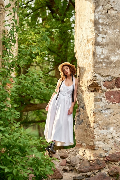 fille dans une robe blanche et un chapeau de paille se tient dans la fenêtre du bâtiment en ruine