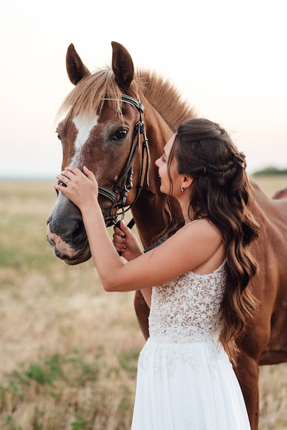 Fille dans une robe blanche à côté d'un cheval brun dans le village